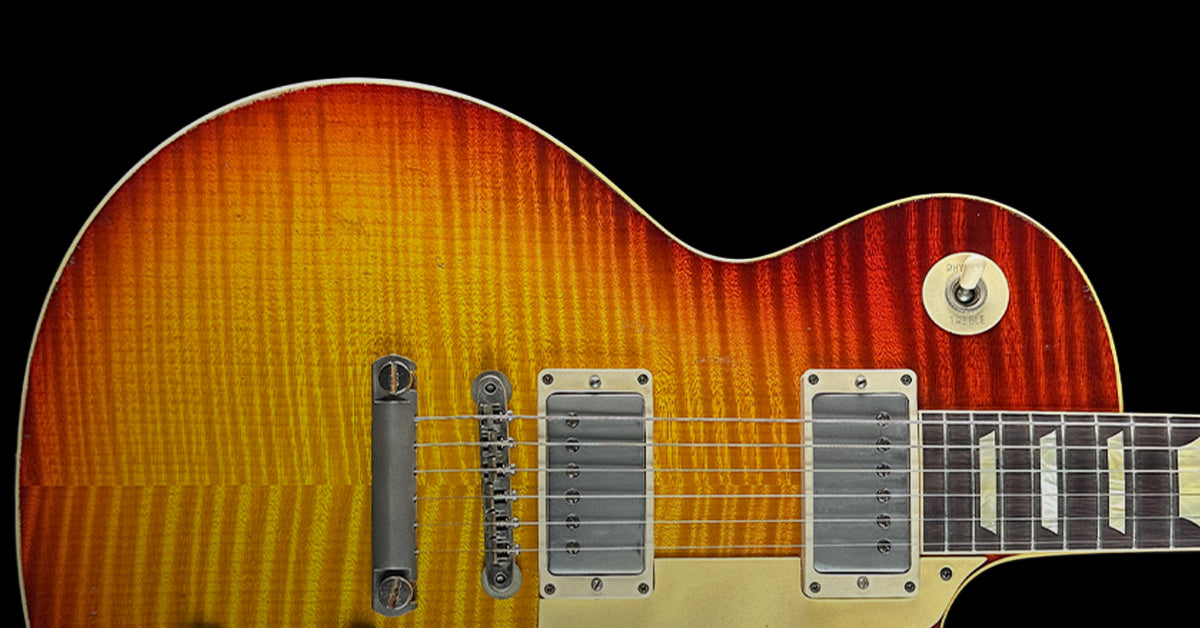 Closeup of cherry sunburst guitar against a black background.