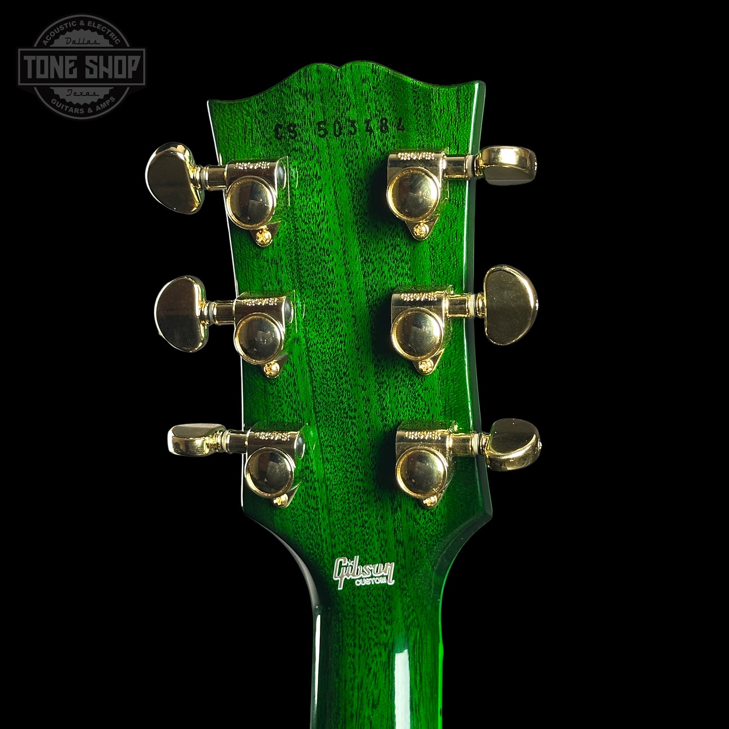 Close-up of a green guitar headstock with tuning pegs on a black background, featuring the Gibson logo.