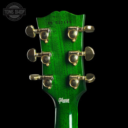 Close-up of a green guitar headstock with tuning pegs on a black background, featuring the Gibson logo.