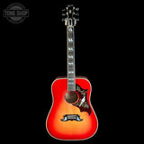 A Gibson acoustic guitar with a vibrant sunburst finish, featuring a red-orange body, a dark fretboard, and intricate bird inlays on the pickguard, set against a solid black background.