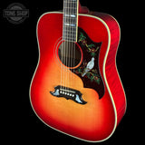 A close-up studio shot of an acoustic guitar against a black background, showing a red-to-orange sunburst finish, a decorative pickguard with a bird and floral motif, and a visible Tone Shop watermark in the upper left.