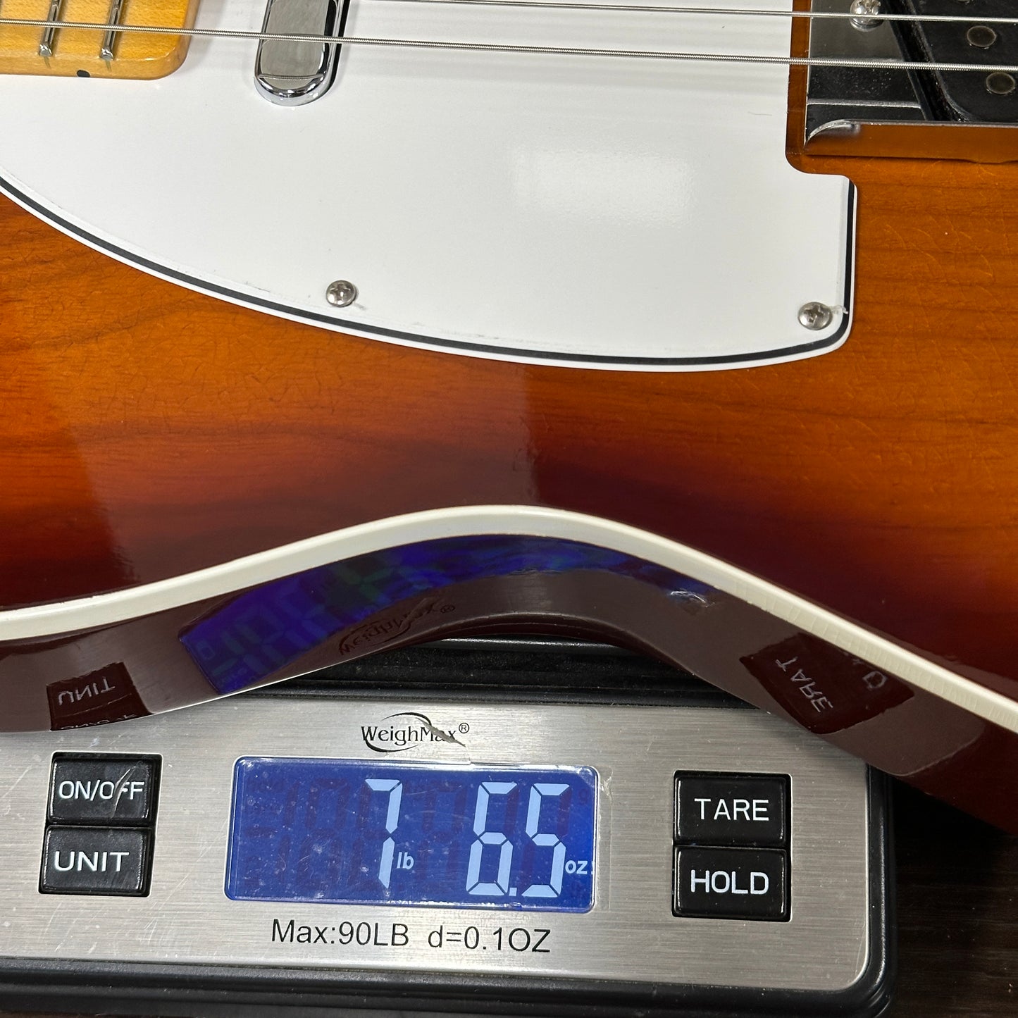Guitar being weighed on a digital scale with a wooden finish.