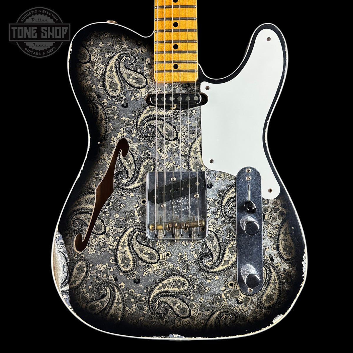 A custom electric guitar with a distressed black and silver paisley pattern on the body, a white pickguard, and a yellow maple neck, shown against a solid black background.