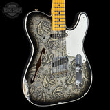 A single-cutaway electric guitar with a distressed black, white, and gray paisley pattern on the body, a white pickguard, and a yellow maple neck, shown against a solid black background.