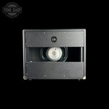 A black guitar speaker cabinet shown from the rear against a solid black background, featuring a textured grille, a cutout revealing a speaker cone, and a Tone Shop watermark in the top left corner.