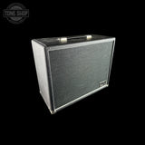 A vintage-style guitar amplifier speaker cabinet with a black textured grille and silver metal trim, shown at an angle on a solid black background. A Tone Shop watermark is visible in the top-left corner.