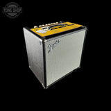 A Guitars & Basses guitar amplifier speaker cabinet with a textured silver grille and a bright yellow top panel, shown on a solid black background with a Tone Shop watermark in the upper left corner.