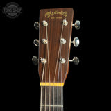 Close-up of the headstock of a Martin & Co acoustic guitar against a black background, showing the brand name in gold, six silver tuning pegs, and a yellow string tree cover.