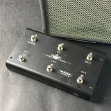 A black Mesa-Boo Triple Down guitar effects pedal with six silver footswitches, shown resting on a dark gray surface next to a speaker grille.