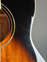 Close-up detail of an acoustic guitar body showing the glossy black outer cover, the warm brown wood inner section, and a thin light-colored binding around the sound hole.