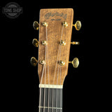 Close-up of the headstock of a Martin & Co acoustic guitar, showing the brand name 'Martin & Co EST. 1930' in gold script on a natural wood background, with six gold tuning pegs and strings against a solid black background.
