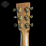 Close-up of the headstock of a guitar with a warm brown wood finish and six gold-toned tuning pegs, shown against a solid black background. A Tone Shop watermark is visible in the top-left corner.