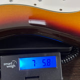 Close-up of a sunburst electric guitar body resting on a digital scale displaying 7.58 kg, with a smart weigh device visible.