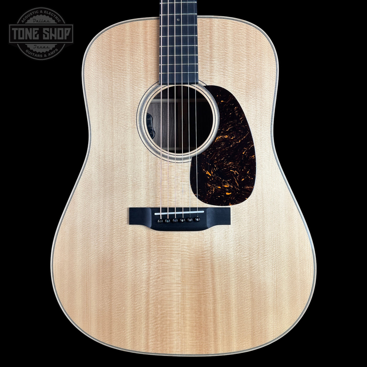 A natural wood acoustic guitar shown from the front against a solid black background, featuring a flamed maple top, dark pickguard, and black bridge. A Tone Shop watermark is visible in the top-left corner.