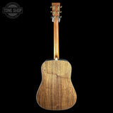 The back of a wooden acoustic guitar, showing the natural wood grain on the backplate and neck, photographed against a solid black background with a Tone Shop watermark in the top left corner.
