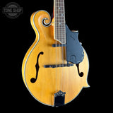 A classic mandolin with a natural honey-amber wood finish, black pickguard, and black bridge, shown against a solid black background. A Tone Shop watermark is visible in the top-left corner.