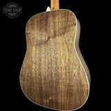 The back of an acoustic guitar with a rich, dark brown wood grain finish, shown against a solid black background with a Tone Shop watermark in the top left corner.