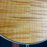 Close-up of a glossy wood surface with a natural flamed grain pattern in warm golden-brown tones, with a thin dark rim visible along the lower edge.