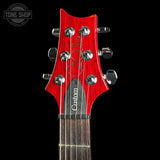 Close-up of the headstock of an electric guitar against a black background, featuring a bright red wood finish, chrome tuning pegs, and a dark fretboard. A Tone Shop watermark is visible in the top-left corner.