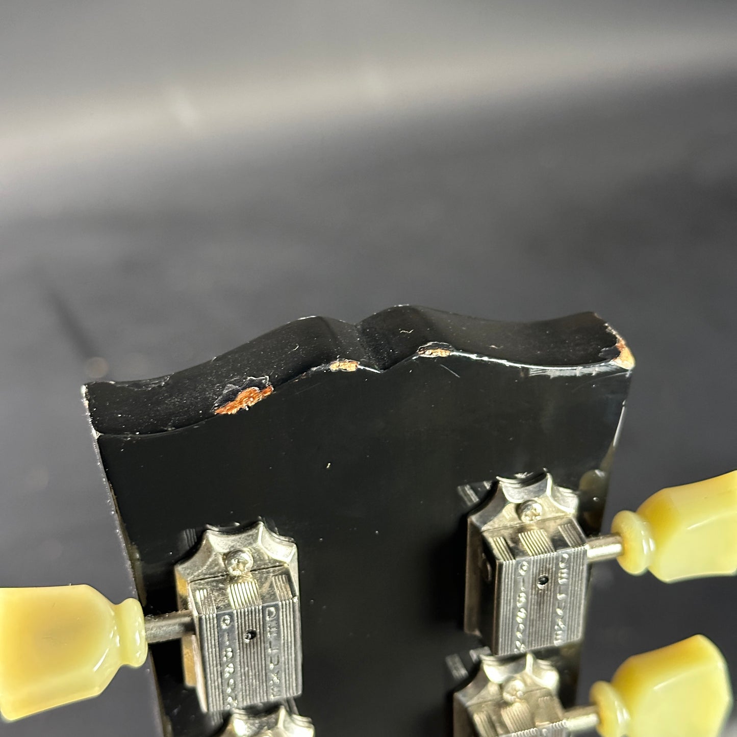 Close-up of a guitar bridge with metal saddles and black block, on a dark background.