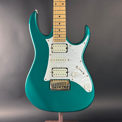 Teal electric guitar on a stand against a gray background