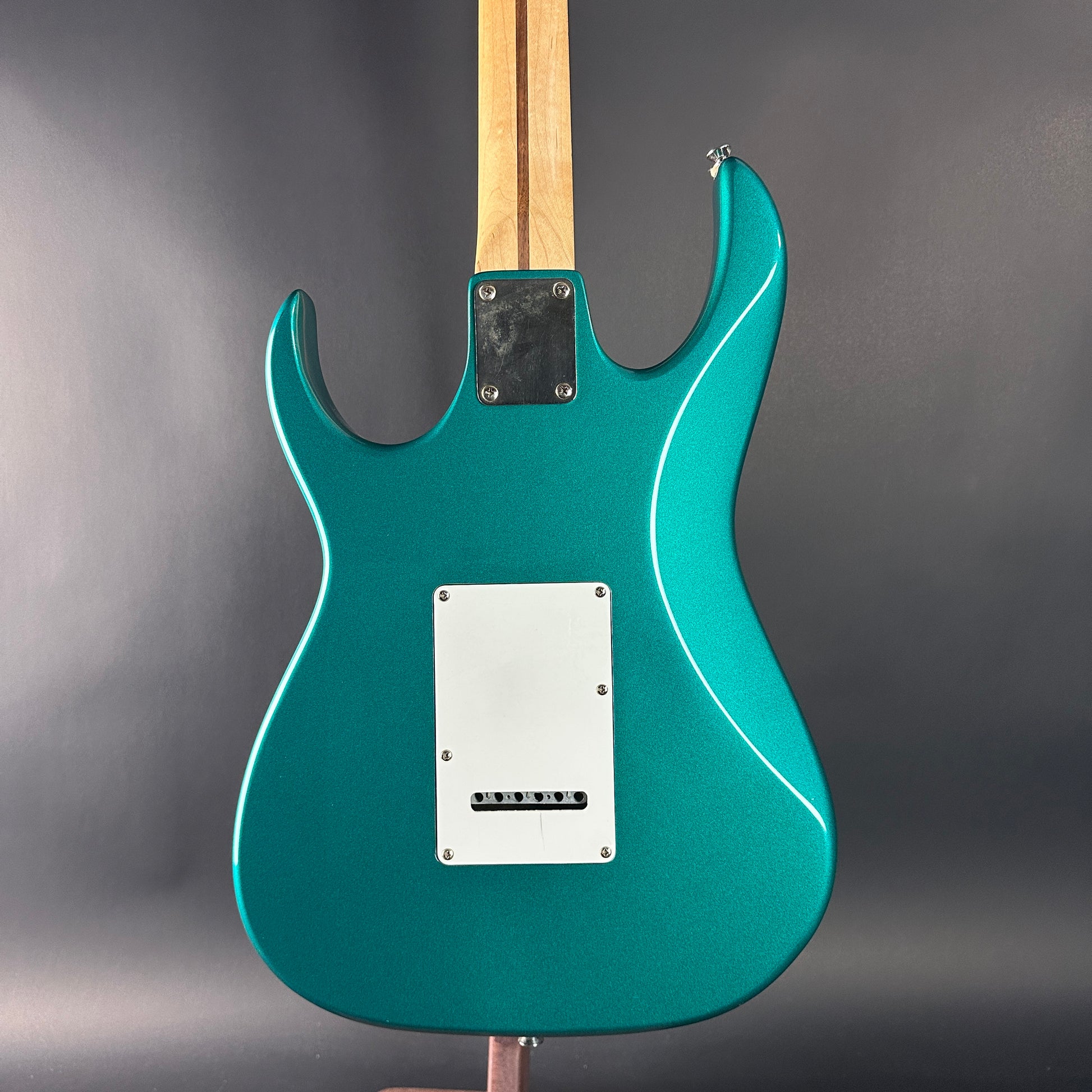 Teal electric guitar on a gray stand with a gray background