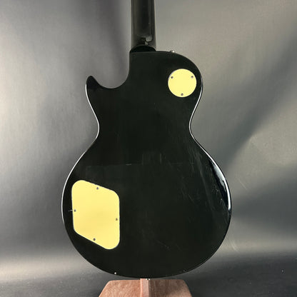 Black electric guitar with gold pickguard on a gray background