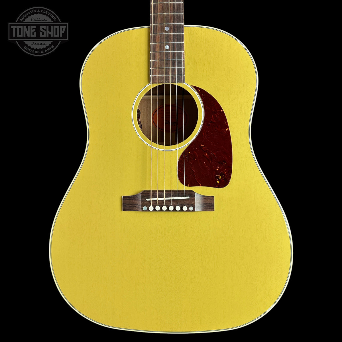 A bright yellow acoustic guitar shown from the front against a solid black background, featuring a dark reddish-brown pickguard and a white binding edge.