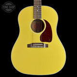 A bright yellow acoustic guitar shown from the front against a solid black background, featuring a dark reddish-brown pickguard and a white binding edge.
