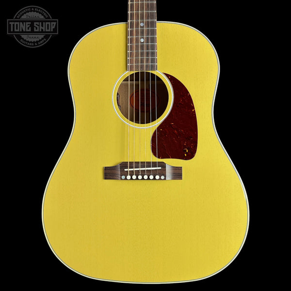A bright yellow acoustic guitar shown from the front against a solid black background, featuring a dark reddish-brown pickguard and a white binding edge.
