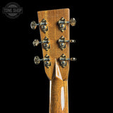 Close-up of the headstock of an acoustic guitar, showing six tuning pegs and a natural wood finish, set against a solid black background with a Tone Shop watermark in the top left corner.