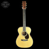 A natural wood acoustic guitar with a cutaway body, shown vertically against a solid black background. A circular 'TONE SHOP' watermark is visible in the top-left corner.