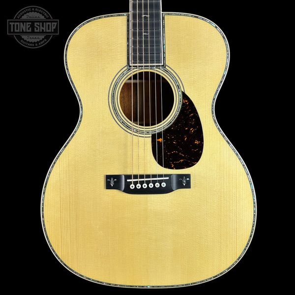 A close-up studio shot of an acoustic guitar body against a solid black background, featuring a natural wood finish, a dark tortoiseshell pickguard, and a black bridge. A 'Tone Shop' watermark is visible in the top-left corner.