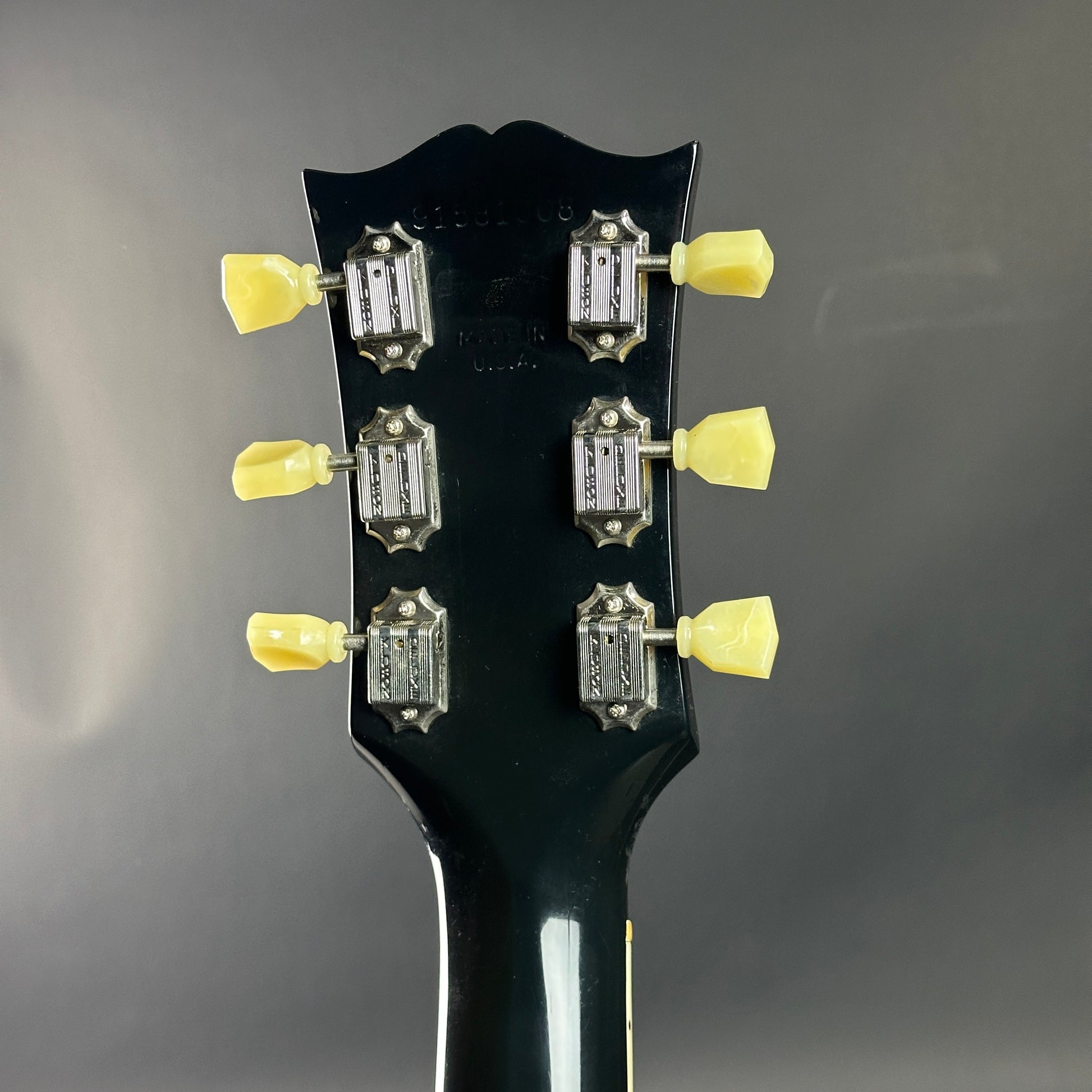 Close-up of a guitar headstock with tuning pegs on a dark background