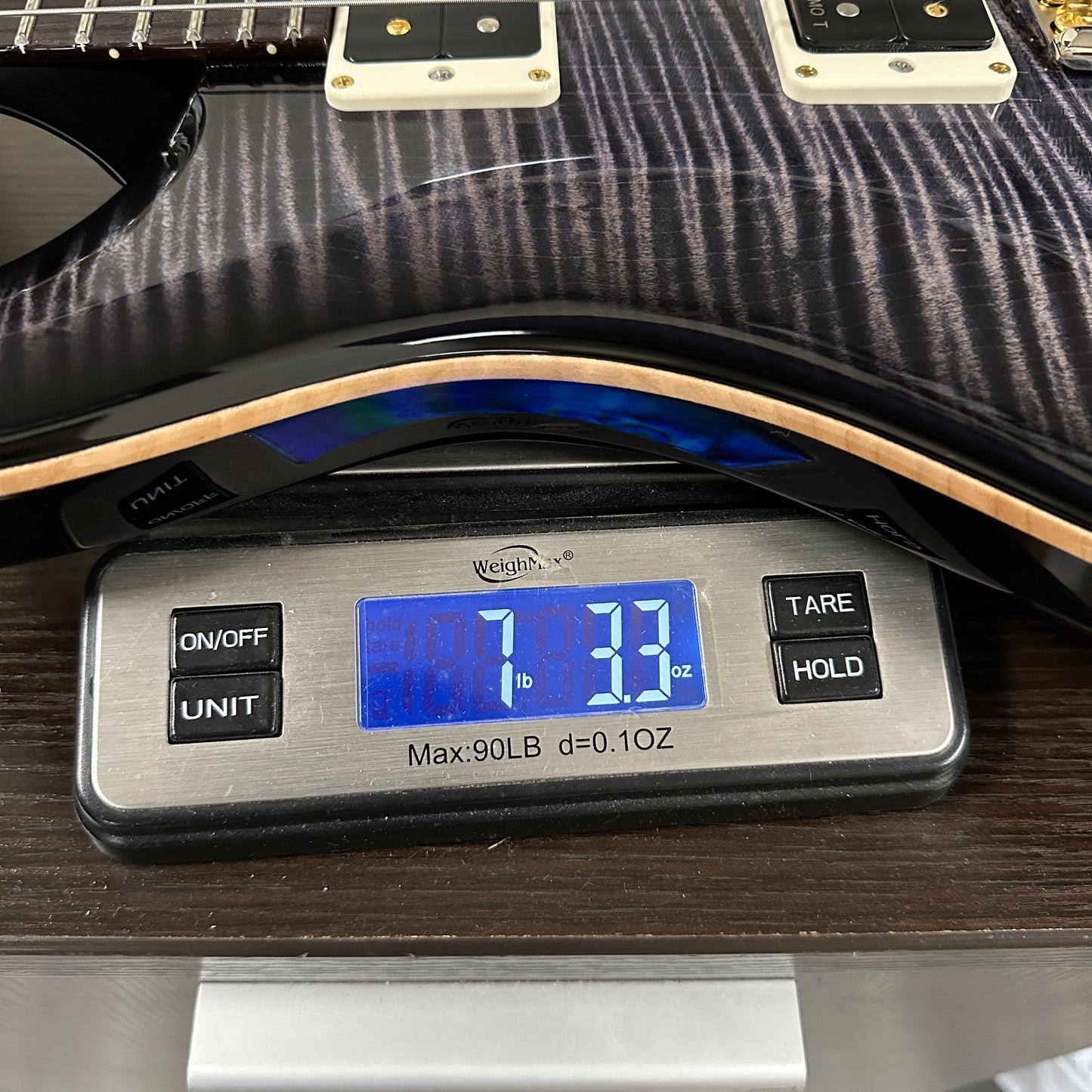 Digital scale displaying weight of a guitar on a wooden surface