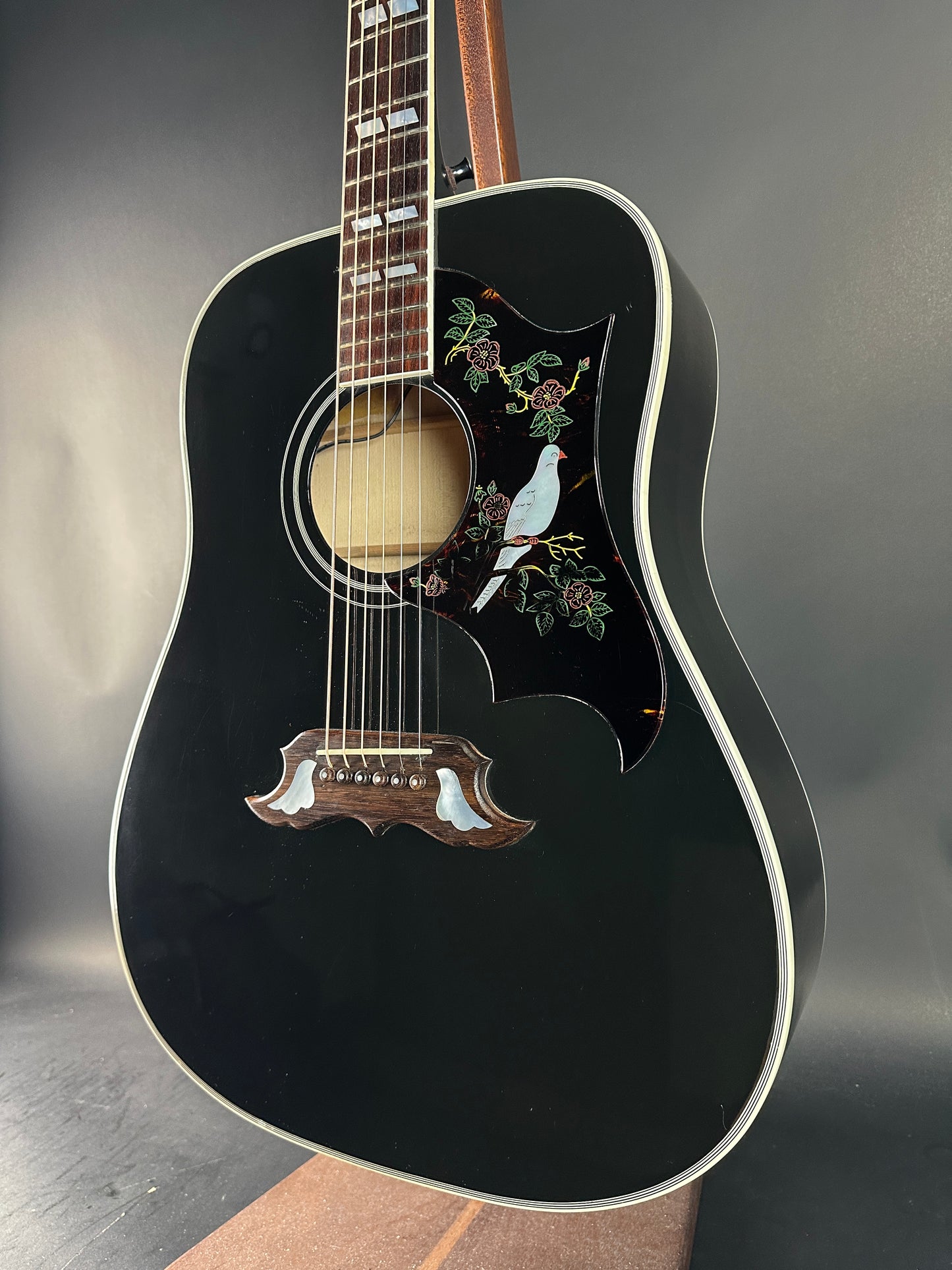 Black acoustic guitar with decorative inlay on a dark surface