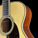Close-up of an acoustic guitar body showing the natural wood soundboard, dark brown sides, and black pickguard against a black background.