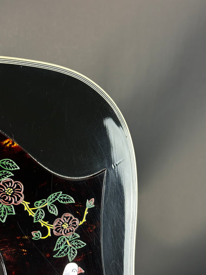 Close-up of a black guitar with pickguard with floral designs on a dark background