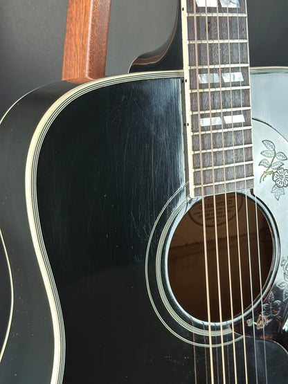 Close-up of a black acoustic guitar with a visible brand logo on the soundhole.