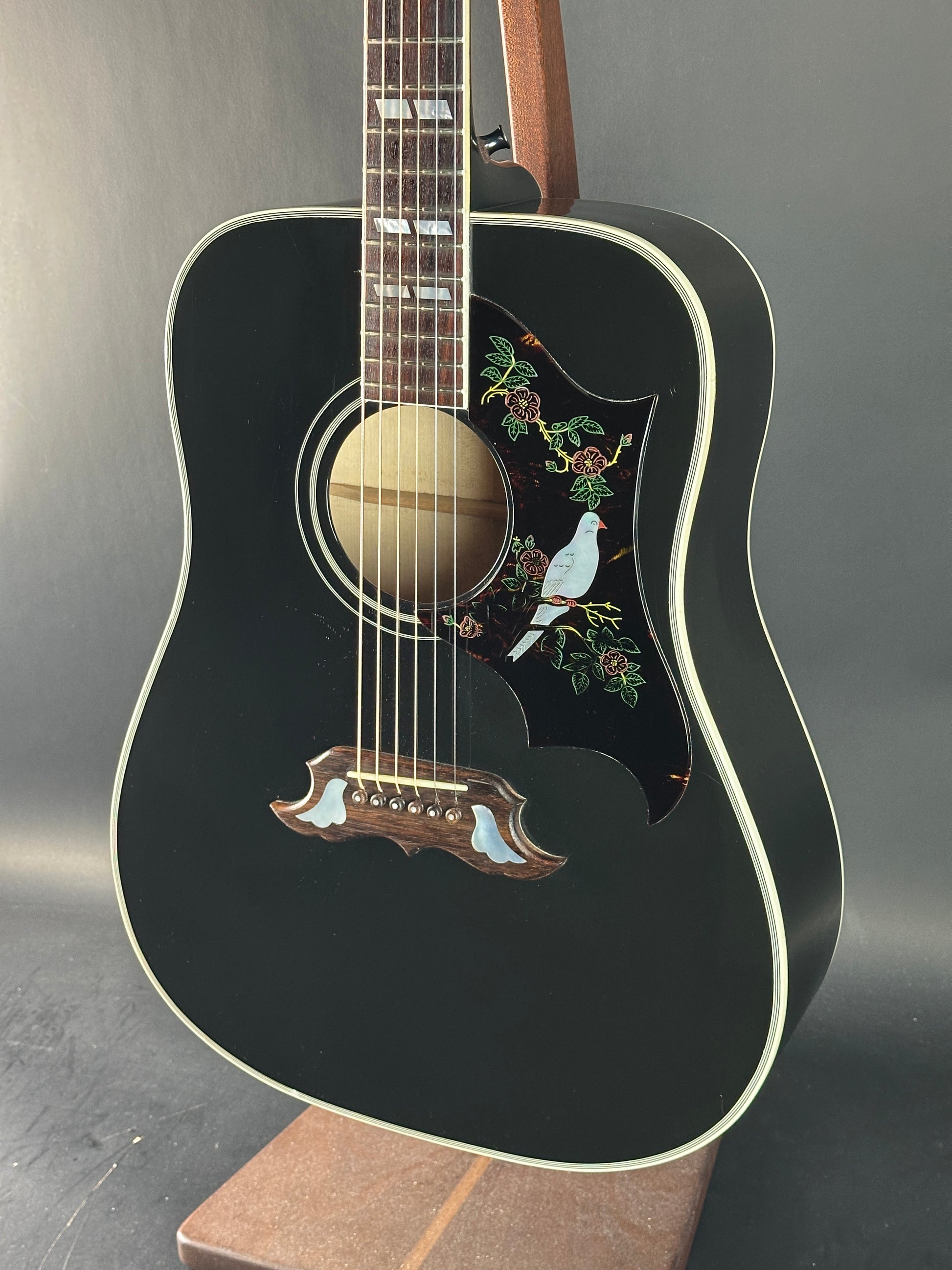 Black acoustic guitar with decorative inlay on a gray background