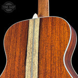 Close-up of the back of an acoustic guitar showing rich wood grain, a central inlay stripe, and white binding against a black background.