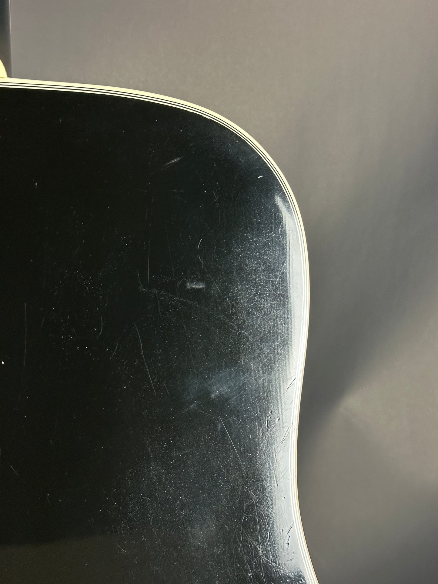 Close-up of a black guitar neck with visible scratches against a dark background