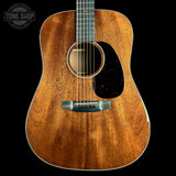 A close-up studio shot of an acoustic guitar body against a solid black background, featuring a warm brown wood grain finish, a black pickguard, and a silver bridge. A 'TONE SHOP' watermark is visible in the top-left corner.