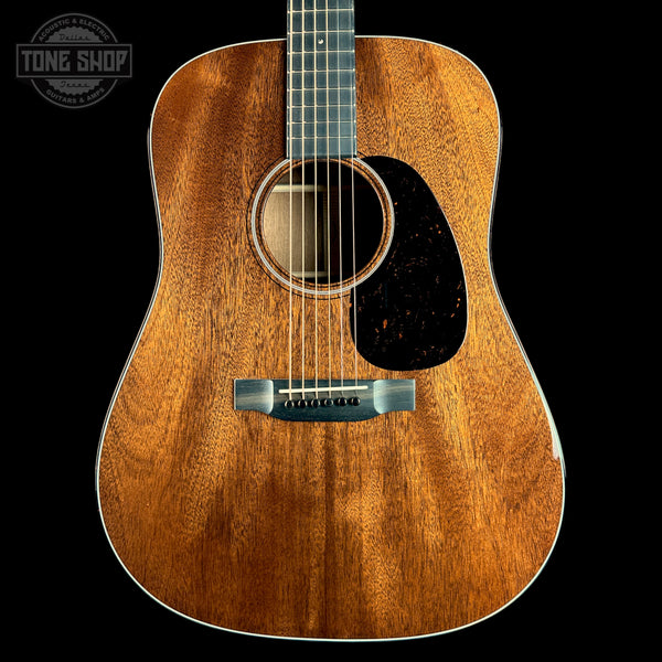 A close-up studio shot of an acoustic guitar body against a solid black background, featuring a warm brown wood grain finish, a black pickguard, and a silver bridge. A 'TONE SHOP' watermark is visible in the top-left corner.
