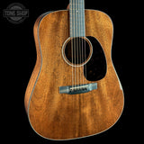 A close-up of a wooden acoustic guitar body with a natural brown wood grain finish, a black pickguard, and a silver-toned bridge, shown against a solid black background. A 'TONE SHOP' watermark is visible in the top left corner.