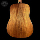 Close-up of the back of a wooden acoustic guitar body, showing the rich grain and warm brown finish against a black background, with a Tone Shop logo in the top left corner.