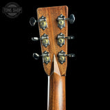 Close-up of the headstock of a wooden acoustic guitar against a solid black background, showing the brand name 'Gibson' on the tuning peg covers.