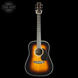A classic acoustic guitar with a sunburst finish, shown from the front against a solid black background. The guitar features a dark brown headstock, a black pickguard, and white binding around the body and neck.