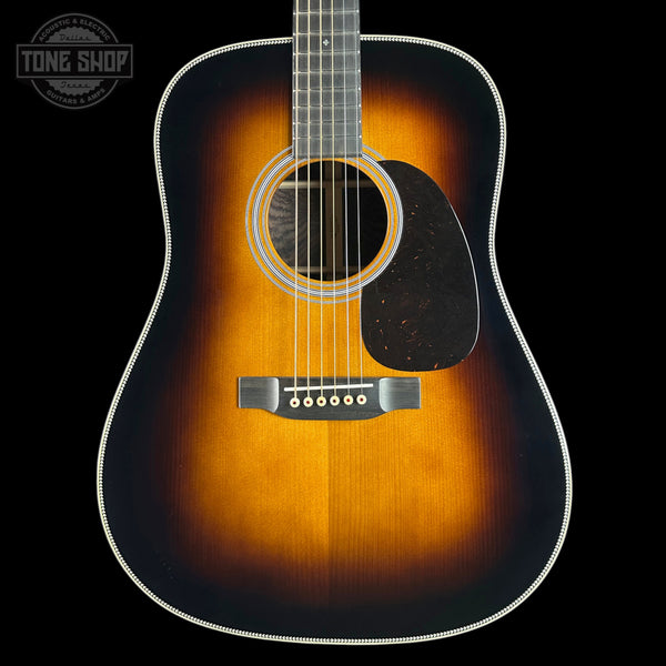 A classic acoustic guitar with a sunburst finish, featuring a dark brown outer edge fading to a bright amber-orange center, set against a solid black background.