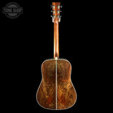 The back of an acoustic guitar with a highly figured wood backplate, shown against a solid black background. A Tone Shop watermark is visible in the top-left corner.